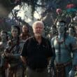 Avatar 3 Vai Fazer História? James Cameron Pode Ser o Primeiro Diretor com 4 Filmes Acima de US$ 1 Bilhão Consecutivos! James Cameron no set de filmagens de Avatar rodeado pelo elenco caracterizado como Na'vi em Pandora, imagem que representa o possível recorde de 4 filmes acima de US$ 1 bilhão em 2025