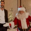 Cena do filme Meu Papai Noel Secreto (2025) com personagem masculino ao lado do Papai Noel em ambiente natalino
