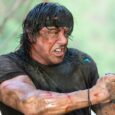 Cena de ação de Rambo com arma e explosões ao fundo, representando sequência removida de Rambo 4